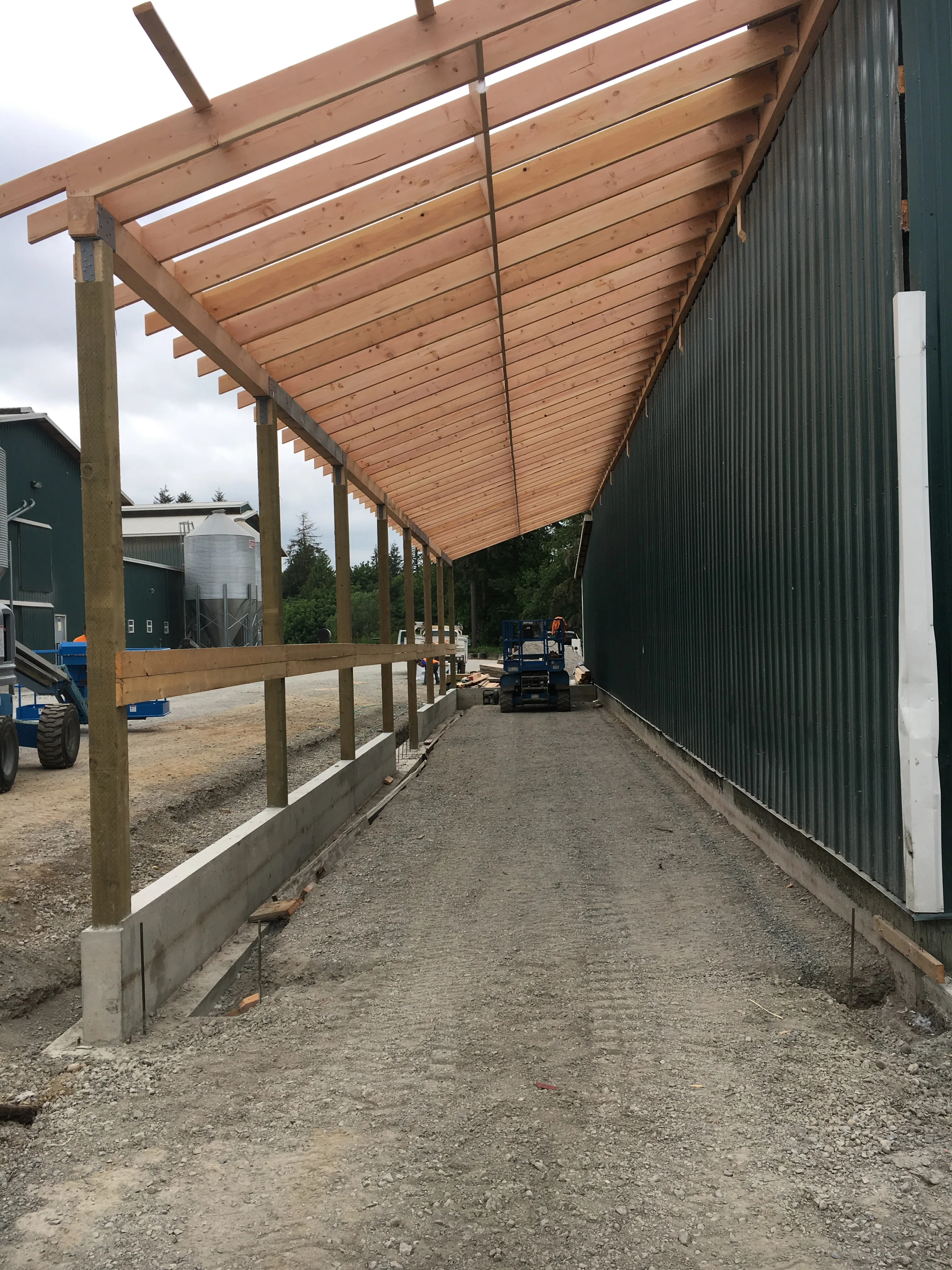 Covered lean-to walkway addition on green metal agricultural building with grain silo