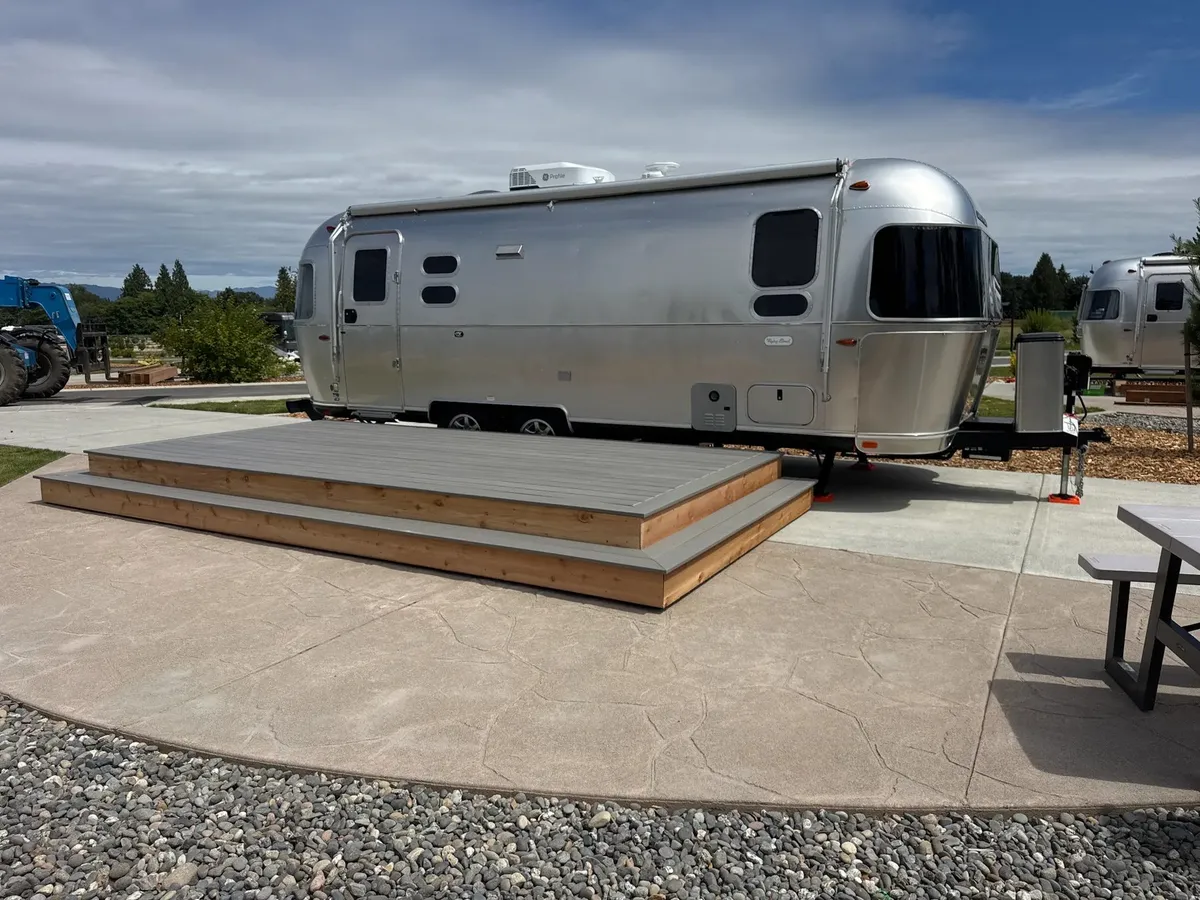 Wide view of a completed composite deck with cedar trim beside a silver Airstream trailer at Angel of the Winds RV Resort in Arlington, Washington, with additional Airstream units visible in the background