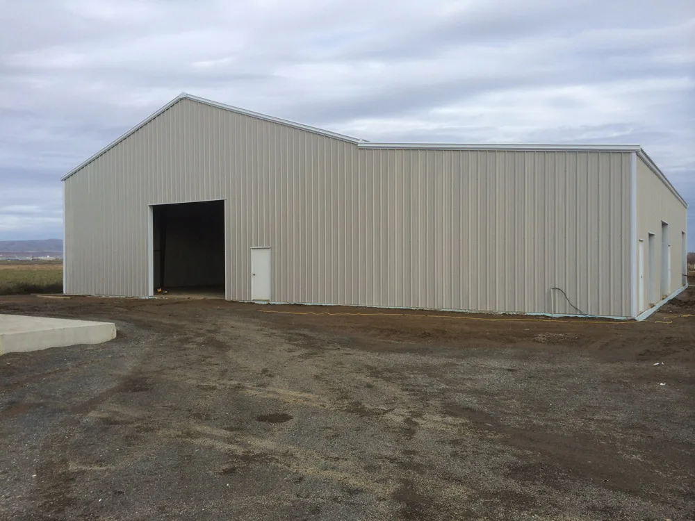 Completed light-colored steel building with large bay door in rural setting